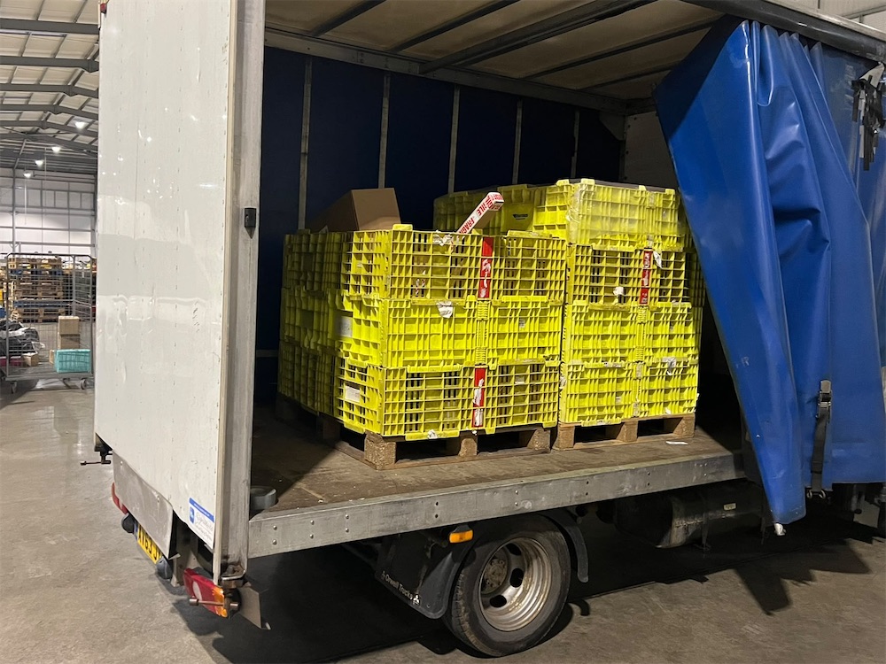 Pallets of yellow crates loaded in the back of a box van inside a warehouse