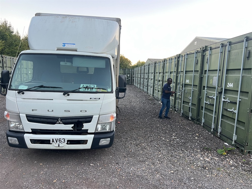A white box van parked by a row of green self-storage containers
