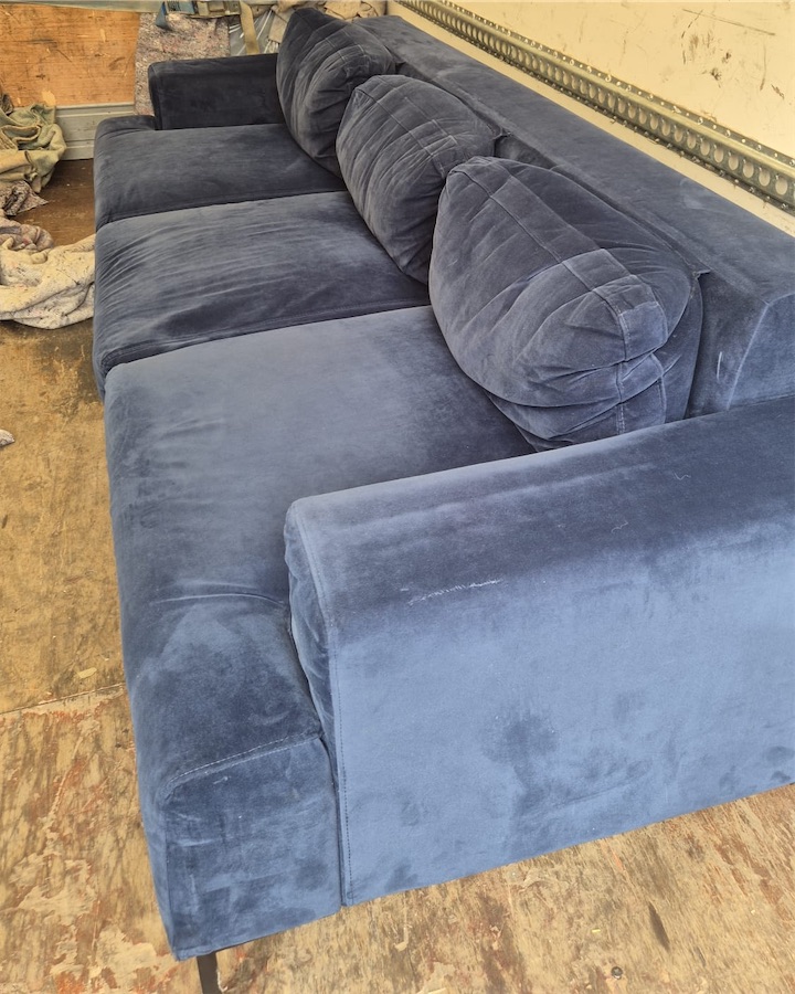 A navy velvet sofa loaded in the back of a Luton van